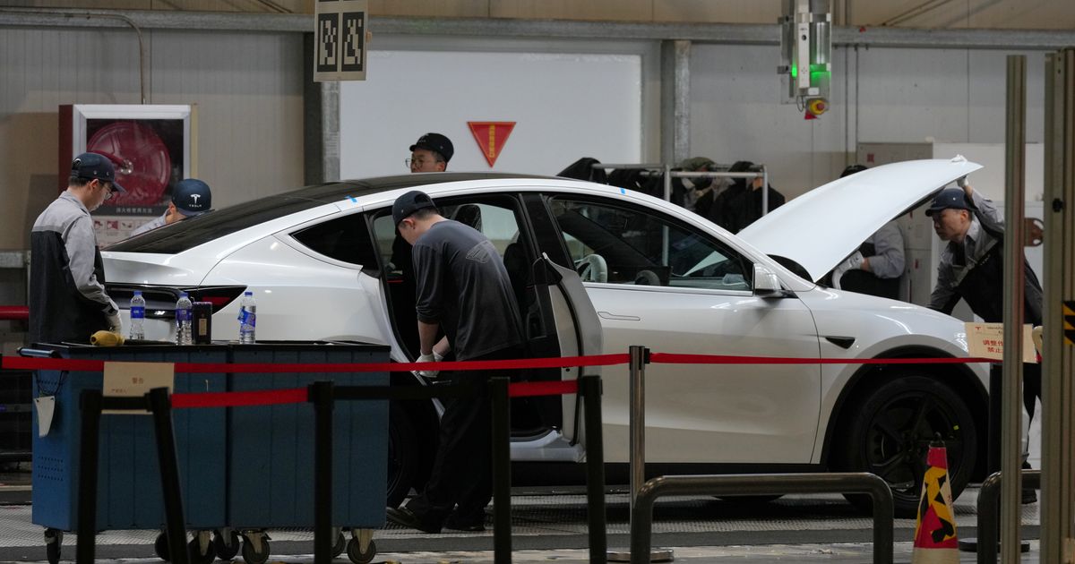 FILE - People work on the Tesla Model Y production line at the Tesla Gigafactory assembly plant during a media organized