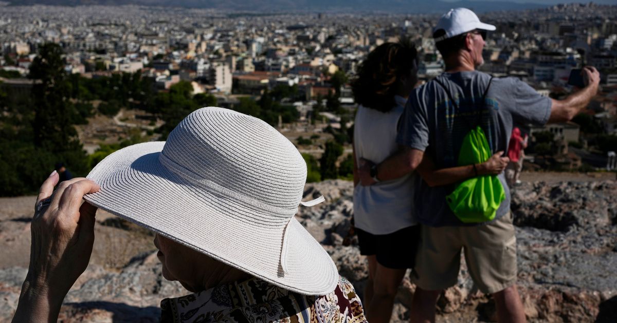 Tourists wearing hats take photographs on the rocky Areios Pagos Hill next to the Acropolis in Athens, Greece, Friday, Aug