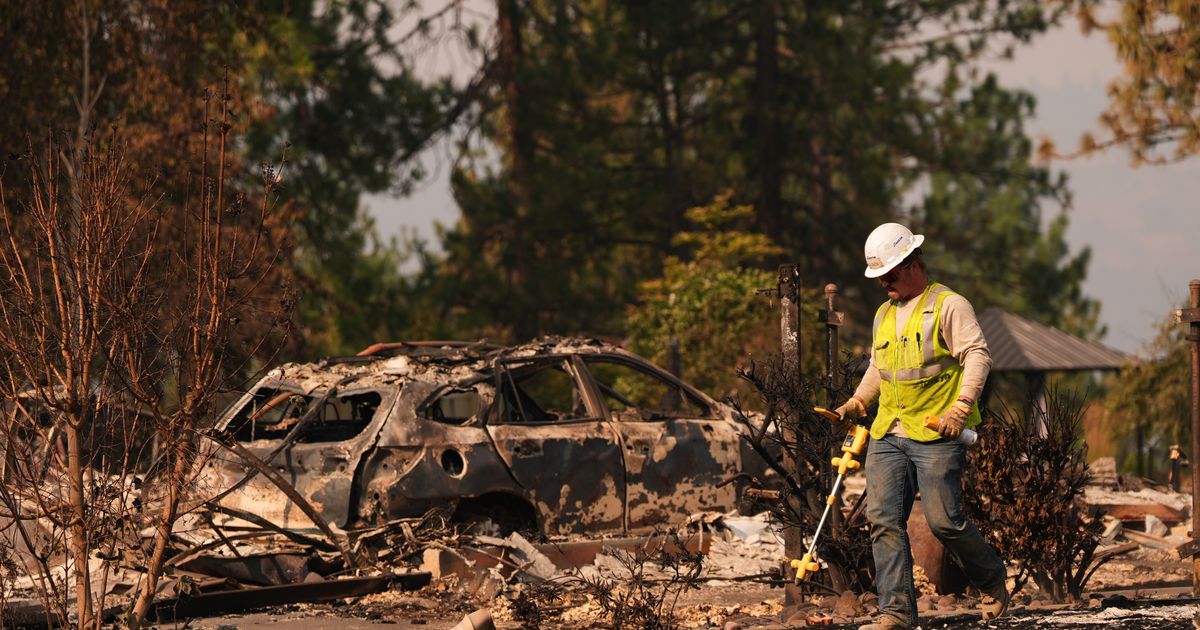 A worker with Avista moves through a property after a wildfire hit the northern part of Spokane, Wash., Monday, Aug. 3