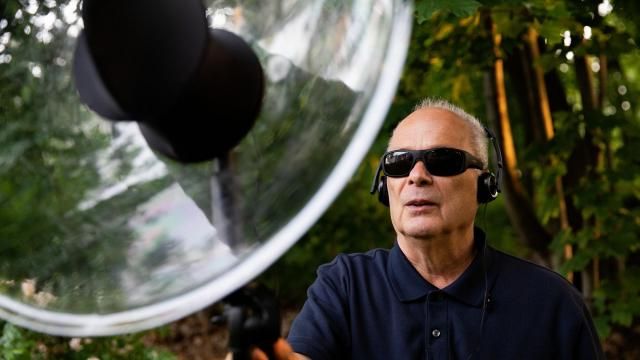 Jerry Berrier uses his amplified parabolic microphone in his backyard in Malden, Mass., June 12, 2023. For some blind birders, avian soundscapes are a way to map the world around them. Increasing noise pollution is imperiling that navigation. (Kayana Szymczak/The New York Times)