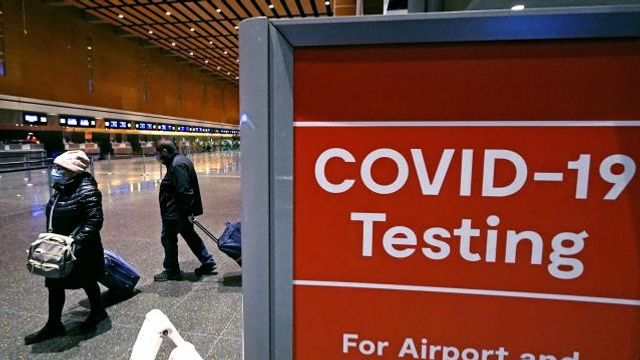 FILE - Travelers pass a sign near a COVID-19 testing site in Terminal E at Logan Airport, on Dec. 21, 2021, in Boston. The nation’s top public health agency is expanding a program that tests international travelers for COVID-19 and other infectious diseases. The Centers for Disease Control and Prevention currently operates a program at six U.S. airports that asks passengers from inbound international flights to agree to nose swabs and answer questions about their travel. (AP Photo/Charles Krupa, File) FILE - Travelers pass a sign near a COVID-19 testing site in Terminal E at Logan Airport, on Dec. 21, 2021, in Boston. The nation’s top public health agency is expanding a program that tests international travelers for COVID-19 and other infectious diseases. The Centers for Disease Control and Prevention currently operates a program at six U.S. airports that asks passengers from inbound international flights to agree to nose swabs and answer questions about their travel. (AP Photo/Charles Krupa, File)