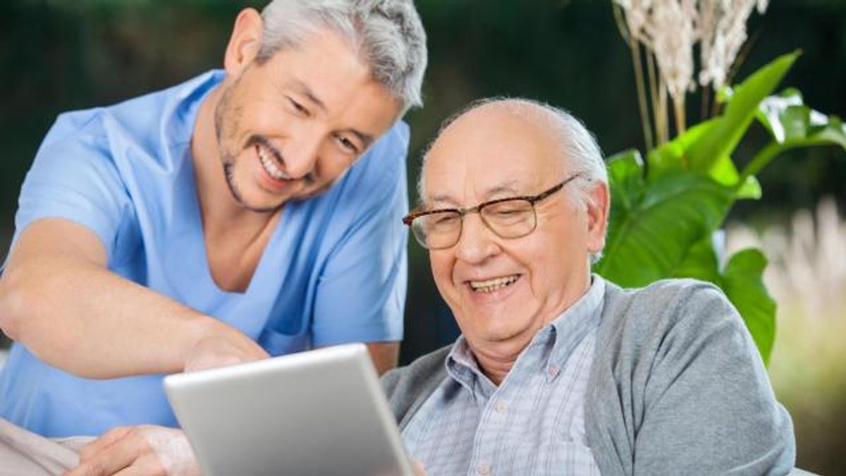 Happy male nurse and senior man enjoying while using tablet comp