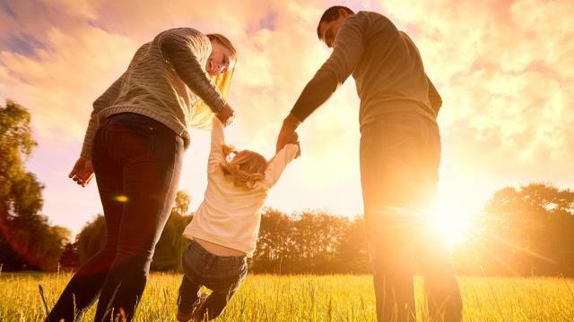 Happy family in the park evening light. The lights of a sun. Mom, dad and baby happy walk at sunset. The concept of a happy family.Parents hold the baby's hands.