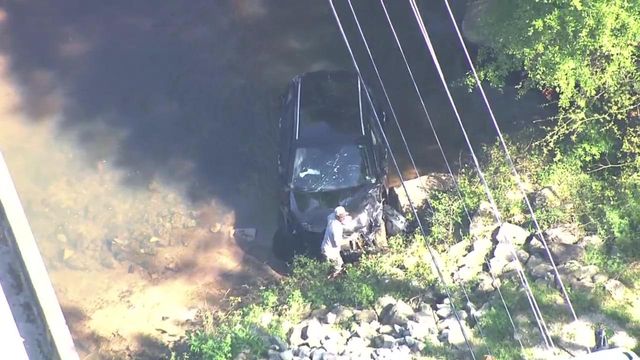 Sky 5 flies over Raleigh creek with partially submerged vehicle 