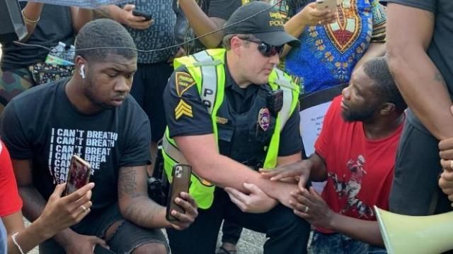 A Fayetteville police officer kneels with protestors.