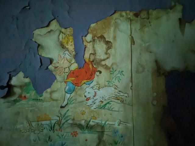 Peeling paint reveals vintage wallpaper beneath.