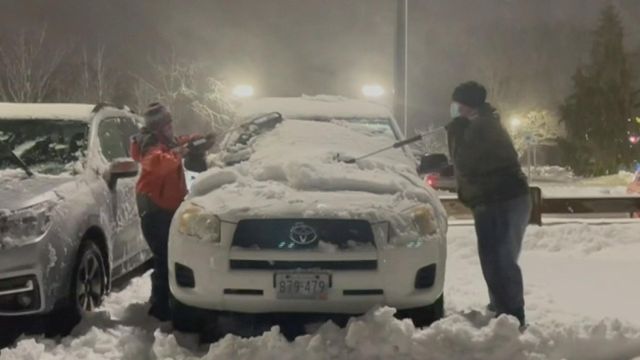 Two good samaritans brush snow off of cars for frontline workers