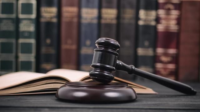 A gavel rests on a desk next to legal books. A gavel rests on a desk next to legal books.