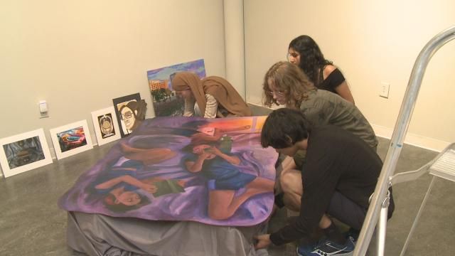 The Greene Level student group helped each other arrange a painting of friends reading books on a bed