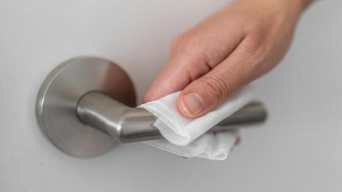 Coronavirus COVID-19 Prevention cleaning woman wiping doorknob with antibacterial disinfecting wipe for killing corona virus on touching surfaces or touching public bathroom handle with tissue.