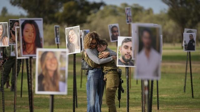 Israelis embrace next to photos of people killed and taken captive by Hamas militants during their violent rampage through the Nova music festival in southern Israel, which are displayed at the site of the event, as Israeli DJs spun music, to commemorate the October 7, massacre, near kibbutz Re'im, Tuesday, Nov. 28, 2023. Nearly two months after Hamas infiltrated Israel, killing some 1,200 people and taking about 240 hostage, dozens are still unaccounted for, their families left living in limbo. (AP Photo/Ohad Zwigenberg)
