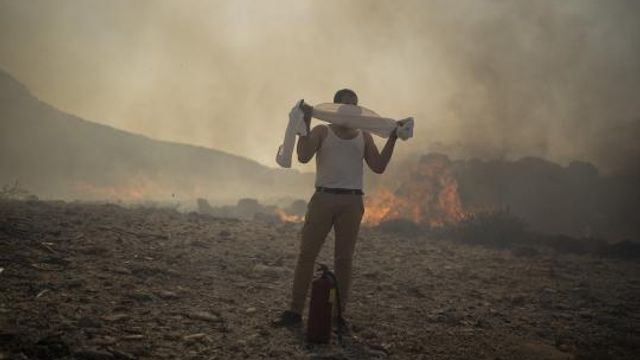FILE - A man wraps his shirt over his face as he tries to extinguish a fire, near the seaside resort of Lindos, on the Aegean Sea island of Rhodes, southeastern Greece, on July 24, 2023. Europe is facing growing climate risks and is unprepared for them, the European Environment Agency said in its first-ever risk assessment for the bloc Monday, March 11, 2024. (AP Photo/Petros Giannakouris, File) FILE - A man wraps his shirt over his face as he tries to extinguish a fire, near the seaside resort of Lindos, on the Aegean Sea island of Rhodes, southeastern Greece, on July 24, 2023. Europe is facing growing climate risks and is unprepared for them, the European Environment Agency said in its first-ever risk assessment for the bloc Monday, March 11, 2024. (AP Photo/Petros Giannakouris, File)