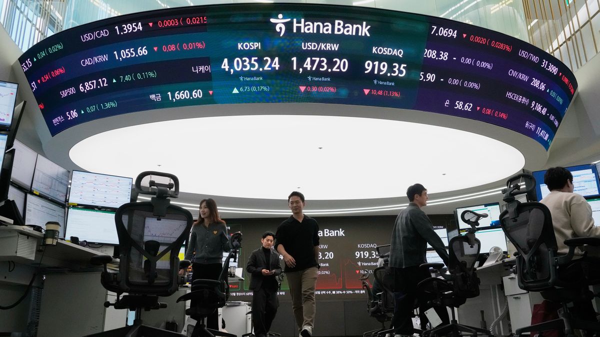 Currency traders pass by a screen showing the Korea Composite Stock Price Index (KOSPI), top center left, and the foreign exchange rate between U.S. dollar and South Korean won, top center, at the foreign exchange dealing room of the Hana Bank headquarters, in Seoul, South Korea, Friday, Dec. 5, 2025. (AP Photo/Ahn Young-joon)