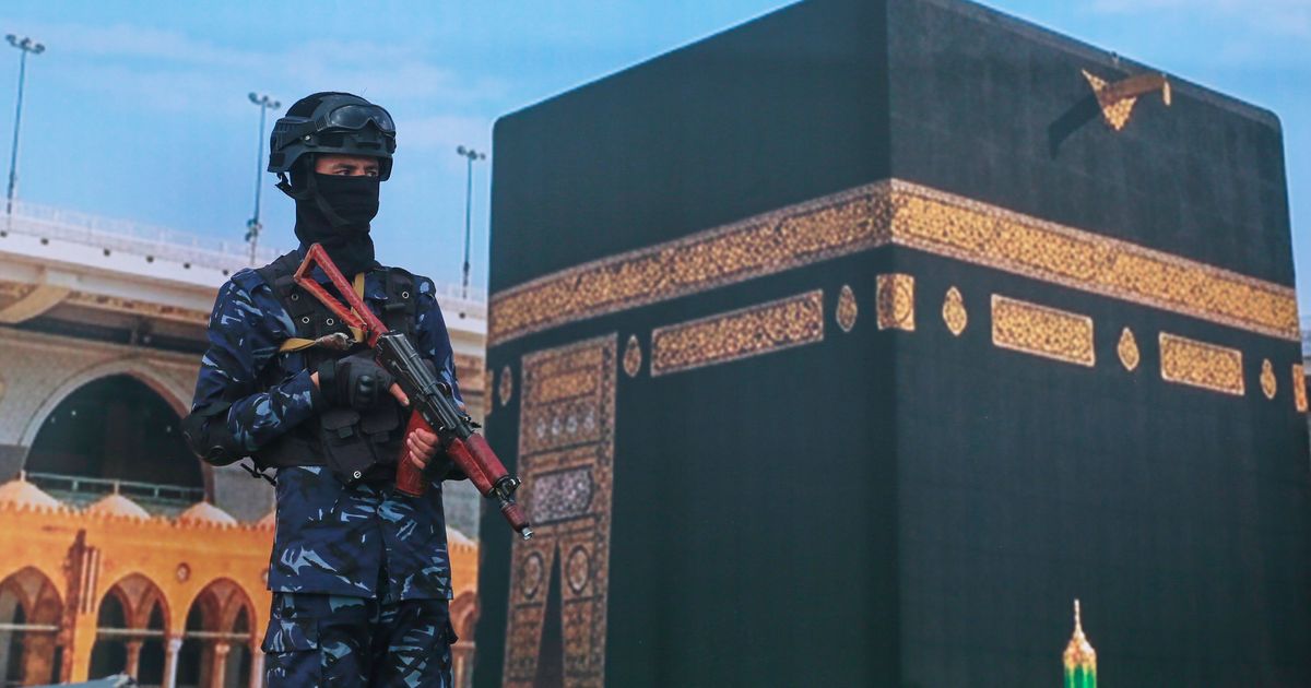 A soldier from Yemen's Houthi rebels stands in front of a giant banner of the Kaaba, during a rally to protest Saudi